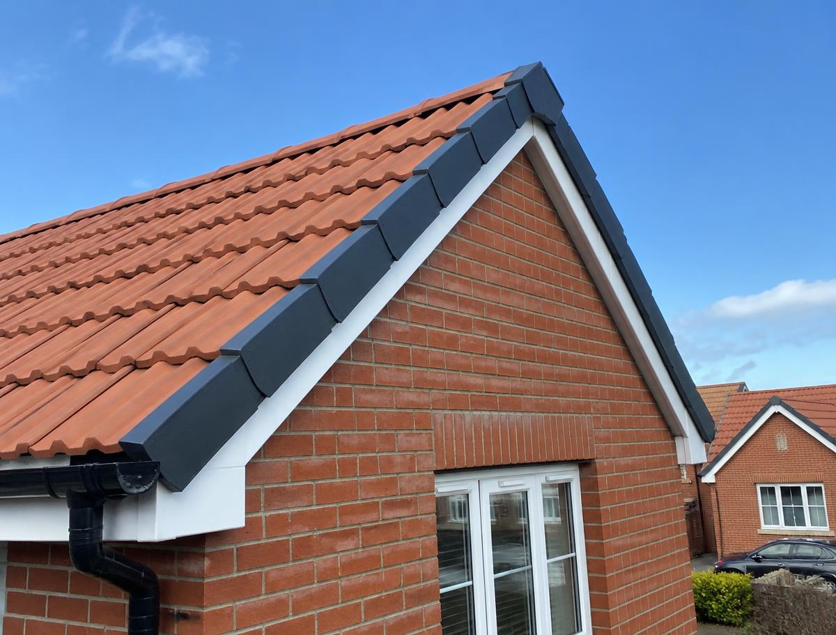 Dark grey dry verge units fitted along the gable of a red-brick house with terracotta roof tiles